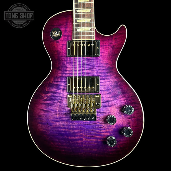 A double-cutaway electric guitar with a vibrant purple and magenta flamed maple top, featuring gold hardware and black pickups, shown against a solid black background.