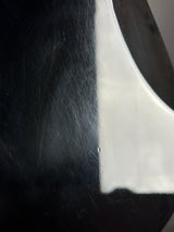 Close-up of a glossy black surface with visible scratches and a bright white highlight along a curved edge.