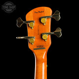 Close-up of the headstock of a bass guitar against a black background, showing the orange wood finish, four black tuning pegs with gold screws, and the brand name Doug Woodard printed on the back.