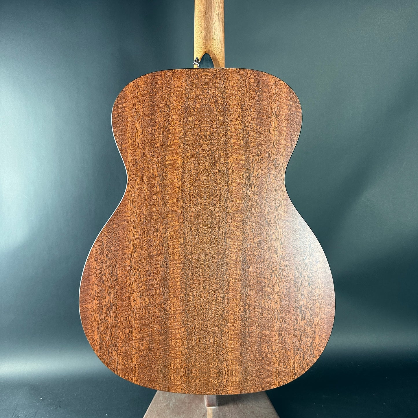 Back view of a wooden acoustic guitar against a dark background