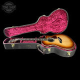 An acoustic guitar with a sunburst finish displayed inside an open hard case with a bright pink velvet interior, set against a solid black background.