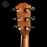Close-up of the headstock of a Taylor acoustic guitar, showing six gold-toned tuning pegs on a dark brown wood finish, set against a solid black background.