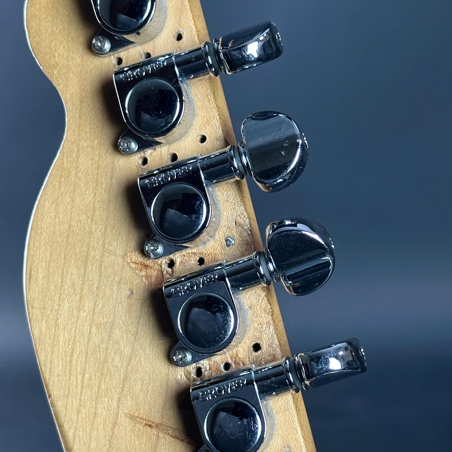 Close-up of a guitar headstock with tuning pegs on a dark background