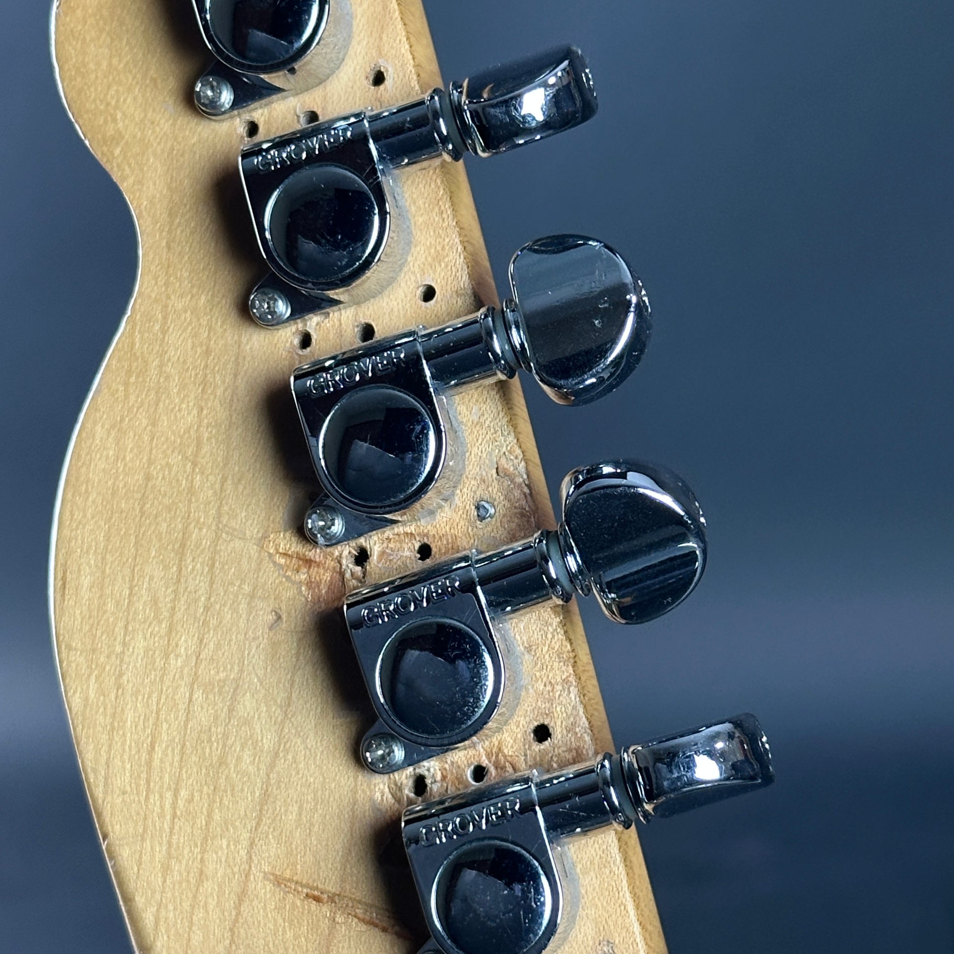 Close-up of a guitar headstock with tuning pegs on a dark background