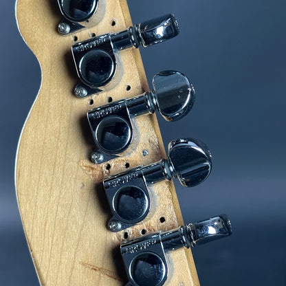 Close-up of a guitar headstock with tuning pegs on a dark background