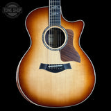 A Taylor acoustic guitar with a natural sunburst finish, shown from the front against a solid black background. The brand logo is visible on the headstock (partially cropped) and the Tone Shop watermark is in the top left corner.
