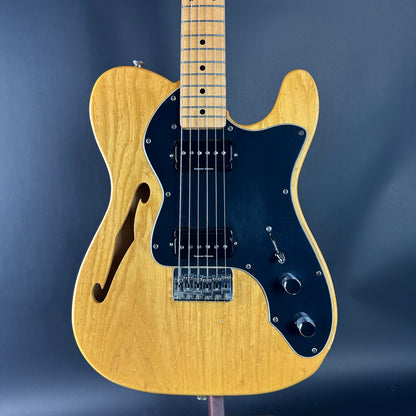 Electric guitar with a black pickguard and natural wood finish on a dark blue background