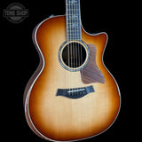 A Taylor acoustic-electric guitar with a natural sunburst finish, shown from a front three-quarter angle against a solid black background. The brand logo 'TONE SHOP' is visible as an overlay in the top-left corner.