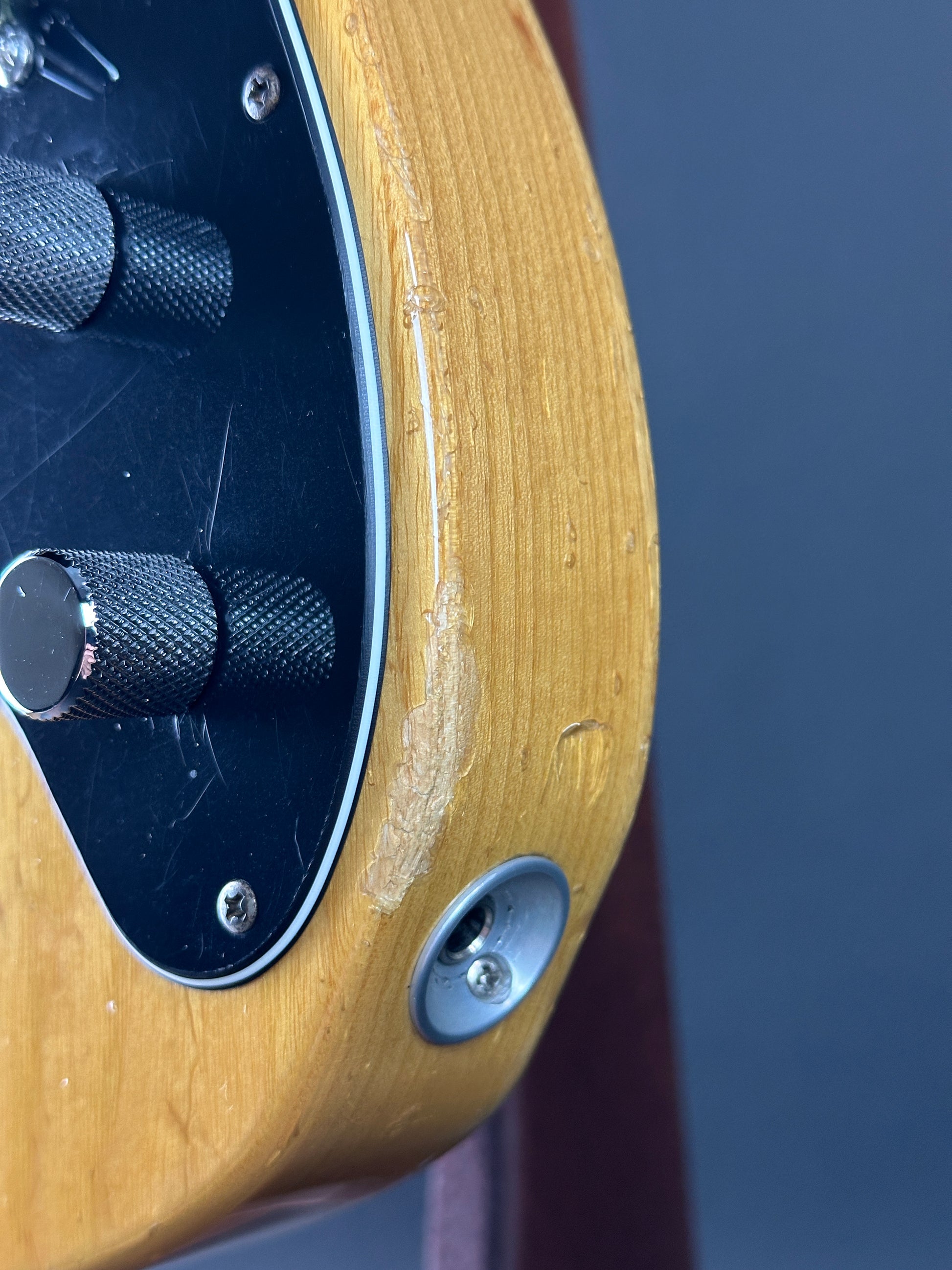 Close-up of a guitar's output jack with wood finish and control knobs.