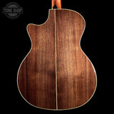 The back of an acoustic guitar with a rich, dark brown wood grain finish and a white binding edge, shown against a solid black background with a Tone Shop watermark in the top left corner.