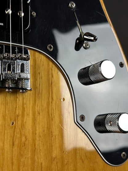Close-up of a guitar's control knobs and headstock on a wooden surface