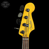 Close-up of a Fender bass guitar headstock in natural yellow wood with four black tuning pegs and strings, shown against a black background with a Tone Shop watermark in the upper left.
