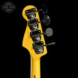 Close-up of the headstock of a yellow-finish bass guitar against a black background, showing four black tuning pegs and a Tone Shop watermark in the upper left corner.