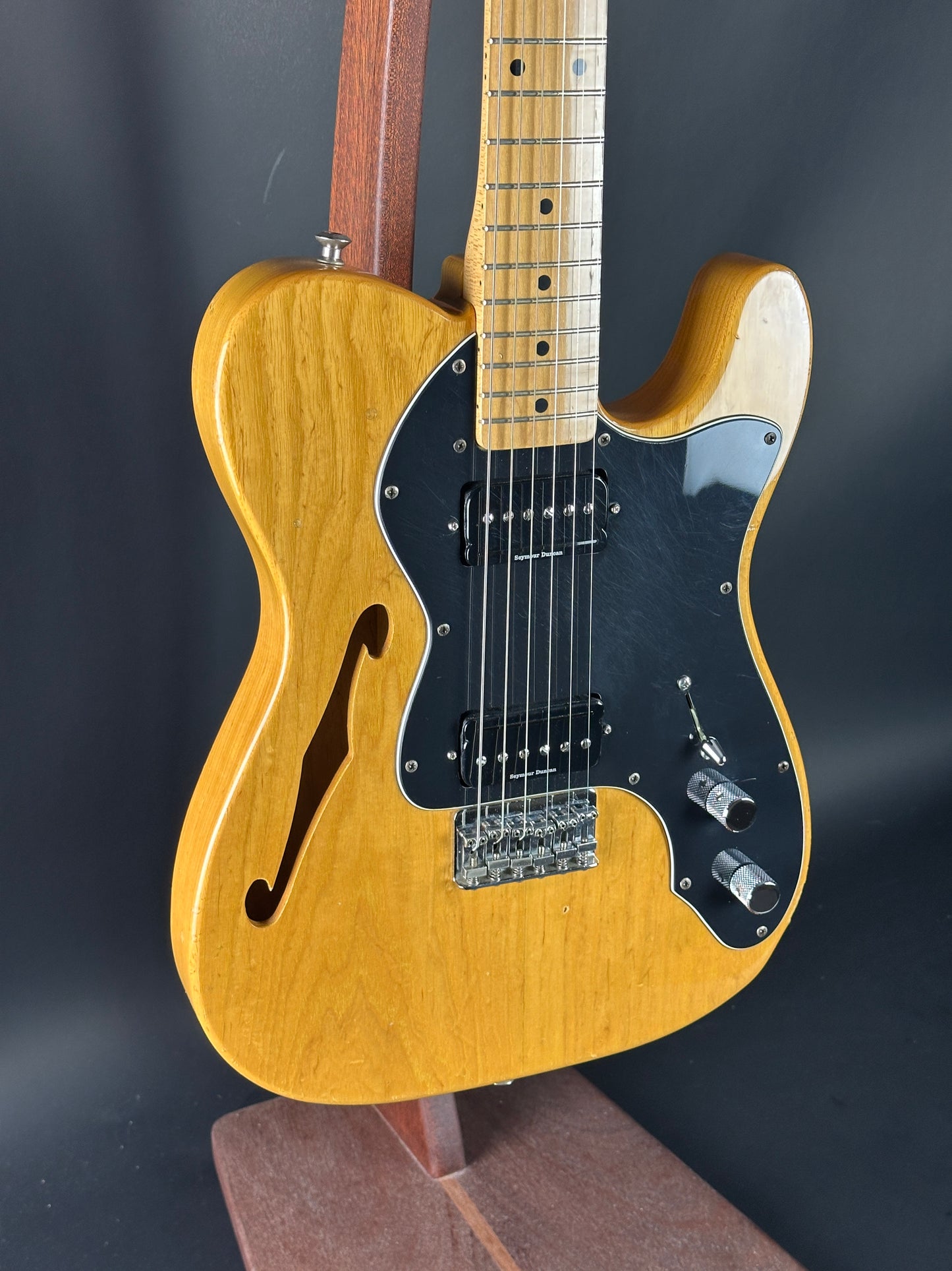Wooden electric guitar with a black pickguard on a dark background