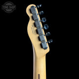 Close-up of the headstock of a Fender Stratocaster electric guitar in a natural maple finish, featuring six black tuners with blue-tinted springs against a solid black background.