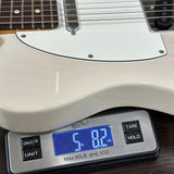 Close-up of a white electric guitar body resting on a digital scale showing 5.82 lbs, with part of the guitar neck and headstock visible at the top.