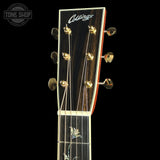 Close-up of the headstock of a Collings acoustic guitar against a black background, showing the brand name, six tuning pegs, and part of the fretboard with floral inlay.