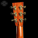 Close-up of the headstock of an acoustic guitar, showing six gold-toned tuning pegs on a glossy reddish-brown wood finish, set against a solid black background.