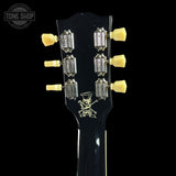Close-up of a black electric guitar headstock with six gold tuning pegs and silver tuning keys, featuring a skull and crossbones logo with the text 'Killer' and 'Guitar'.