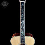 Close-up of the neck of an acoustic guitar with floral inlay on the fretboard, shown against a black background. A Tone Shop watermark is visible in the top left corner.