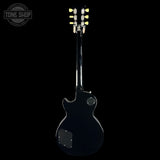 A black electric guitar shown from the back against a solid black background, with a Tone Shop watermark in the upper left corner.