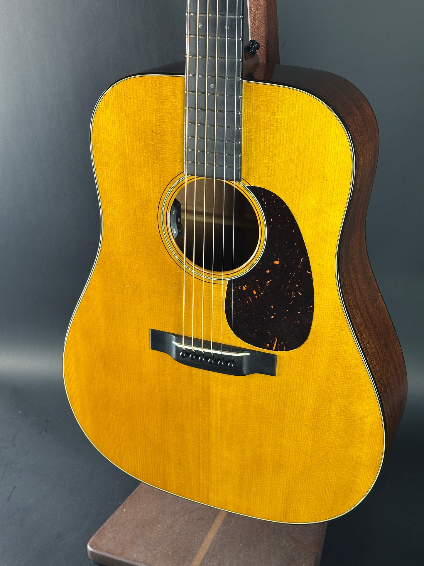 Acoustic guitar with a wooden body and brown pickguard on a dark background