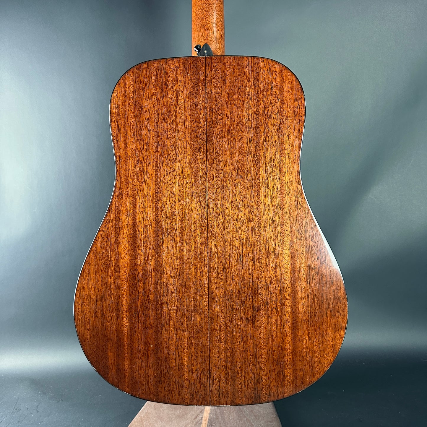 Back view of a wooden acoustic guitar on a gray background