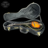 A St. Luc mandolin resting inside an open black hard case with gold-tone latches, photographed on a solid black background.