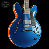 Blue electric guitar with a black pickguard on a black background, featuring the Tone Shop logo.