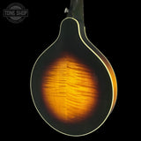 Close-up of the back of an acoustic guitar showing a dark sunburst finish that transitions to a warm amber-orange wood grain, set against a solid black background with a Tone Shop watermark in the top left.