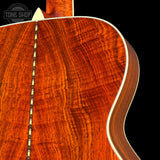 Close-up of the back of an acoustic guitar showing a rich, warm reddish-brown wood grain finish with a decorative inlay running vertically down the center, set against a solid black background.