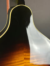 Close-up of the back of an acoustic guitar showing the glossy dark top, natural wood edge, and a warm brown sunburst gradient on a dark gray background.