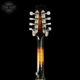 Close-up of the headstock and upper neck of a six-string acoustic guitar against a solid black background. The headstock features a glossy black finish with a warm orange-brown sunburst gradient along the neck, silver hardware, and white tuning pegs.