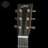 Close-up of the headstock of a Collings acoustic guitar against a black background, showing the brand name in gold script, six silver tuning pegs, and part of the dark wood neck.
