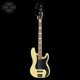 A Fender bass guitar with a cream-colored body, black pickguard, and dark wood fretboard, shown vertically against a solid black background. A Tone Shop watermark is visible in the top-left corner.