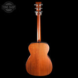 The back of a wooden acoustic guitar, showing the rich grain of the mahogany-style backplate and neck, photographed against a solid black background with a Tone Shop watermark in the top left corner.