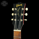 Close-up of the headstock of a Gibson Junior Les Paul electric guitar, showing the black wood headstock with gold lettering, six cream tuning pegs, and the neck beginning below, set against a solid black background.