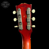 Close-up of the headstock of a vintage acoustic guitar with a red sunburst finish, showing six white tuning pegs and silver tuning keys against a black background.