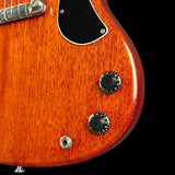 Close-up of an electric guitar body showing a glossy reddish-orange wood finish, black pickguard, two black control knobs, and a silver metal screw terminal against a black background.
