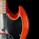 Close-up of a classic electric guitar body featuring a glossy red-orange sunburst finish, a black pickguard, and a dark fretboard against a solid black background.