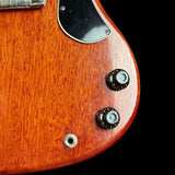 Close-up of a reddish-orange wood guitar body with a black pickguard and black control knobs on a black background.