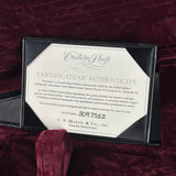 A Martin Custom Shop guitar certificate of authenticity displayed in a black presentation frame on a deep burgundy velvet surface. The certificate features a cream-colored octagonal center with black text and is branded with the Martin logo.