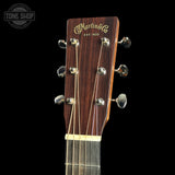 Close-up of the headstock of a Martin & Co acoustic guitar against a solid black background, featuring the brand name in gold script and six silver tuning pegs.