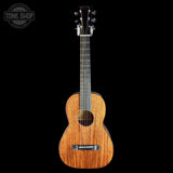 A wooden acoustic guitar with a warm honey-toned wood finish and dark headstock, photographed upright against a solid black background. A circular 'TONE SHOP' watermark is visible in the top-left corner.