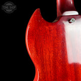 Close-up of the glossy red wood back of an electric guitar against a black background, showing the wood grain and a small silver screw near the neck joint.