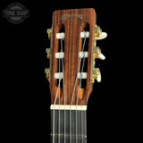 Close-up of the headstock of a Martin & Co classical guitar against a solid black background, showing the wooden headstock, tuning pegs, and strings.