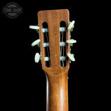 Close-up of the headstock of an acoustic guitar, showing the six white tuning pegs and strings against a solid black background. A 'TONE SHOP' watermark is visible in the top left corner.