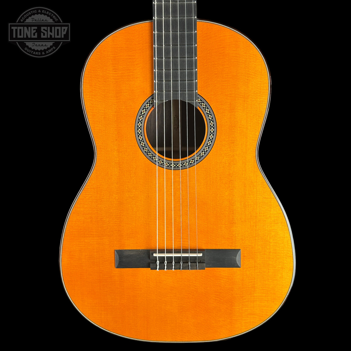 A classic acoustic guitar with a bright orange-yellow spruce top, black headstock, and decorative rosette, shown against a solid black background with a Tone Shop watermark in the top left corner.