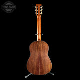 The back of an acoustic guitar with a rich, dark brown wood grain finish, displayed on a black background with a Tone Shop watermark in the top left corner.