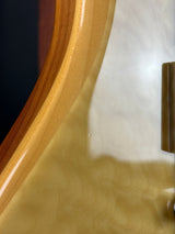 Close-up detail of a glossy wood instrument body edge with a flamed maple pattern in warm natural wood tones.